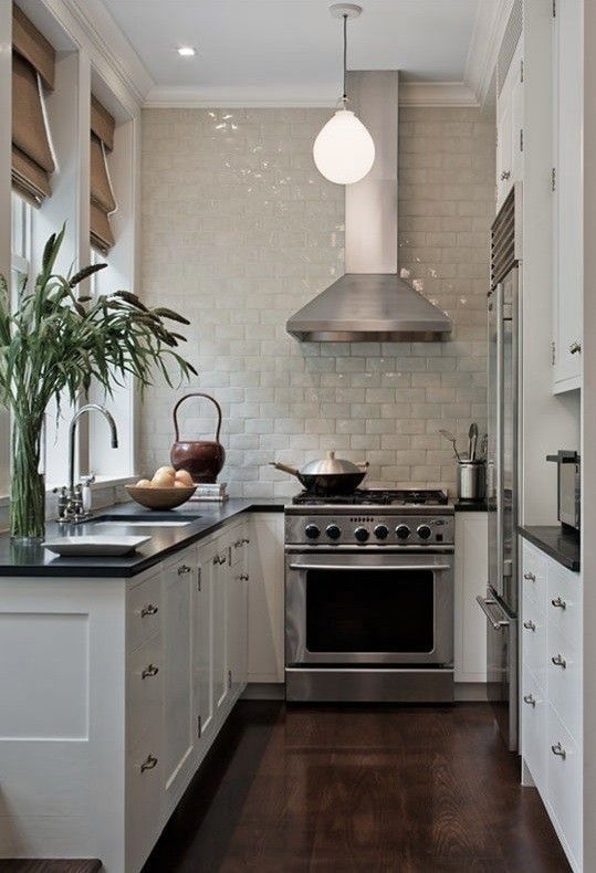 a white U-shaped kitchen with black countertops, a neutral tile backsplash and some greenery is a cozy little space