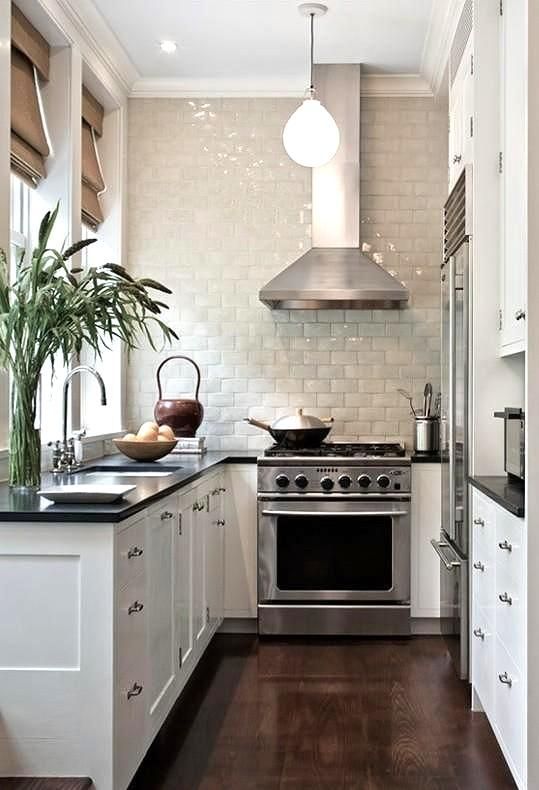 A white farmhouse U shaped kitchen with a black countertop, a glazed tile backsplash and stainless steel appliances