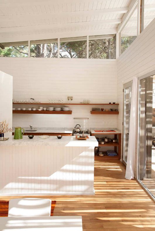 a white farmhouse kitchen with beadboard cladding the walls and clerestory windows that bring light inside and sliding doors