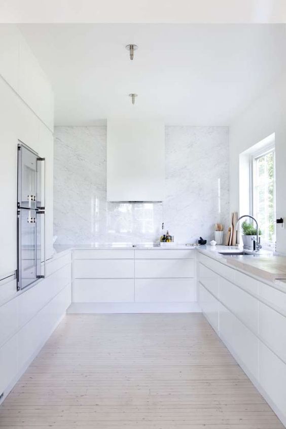 a white minimalist kitchen with a white stone backsplash plus countertops is a very airy and serene space
