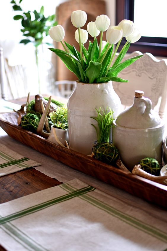 a wooden box with moss balls, grass and greenery, a vase with white tulips and antlers for a rustic spring table