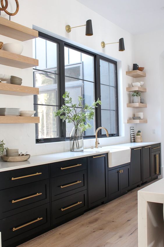 an elegant black farmhouse kitchen with open floating shelves, a white backsplash and countertop plus brass touches