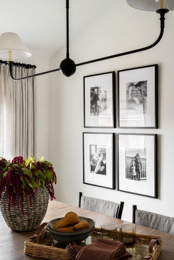 an elegant dining room with a black and white grid gallery wall, a stained table and chairs, a cool chandelier
