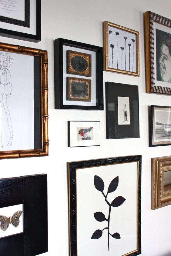 an elegant free form gallery wall with gold and black frames and black and white artworks is very chic