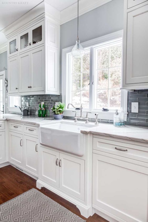 an elegant vintage white kitchen with shaker cabinets, white quartz countertops, a grey glossy tile backsplash and stainless steel touches