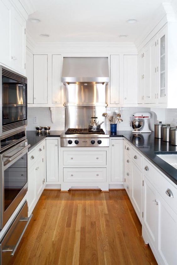 An elegant white U shaped kitchen with black coutnertops and a white tile backsplash plus shiny appliances