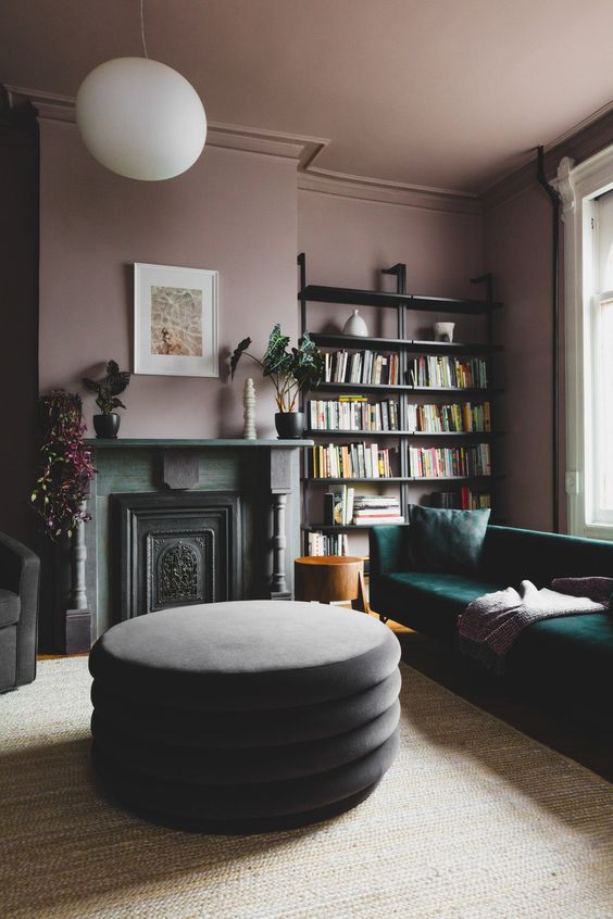 an exquisite living room with mauve walls and a ceiling, open shelves, a green sofa, a non-working fireplace and potted plants