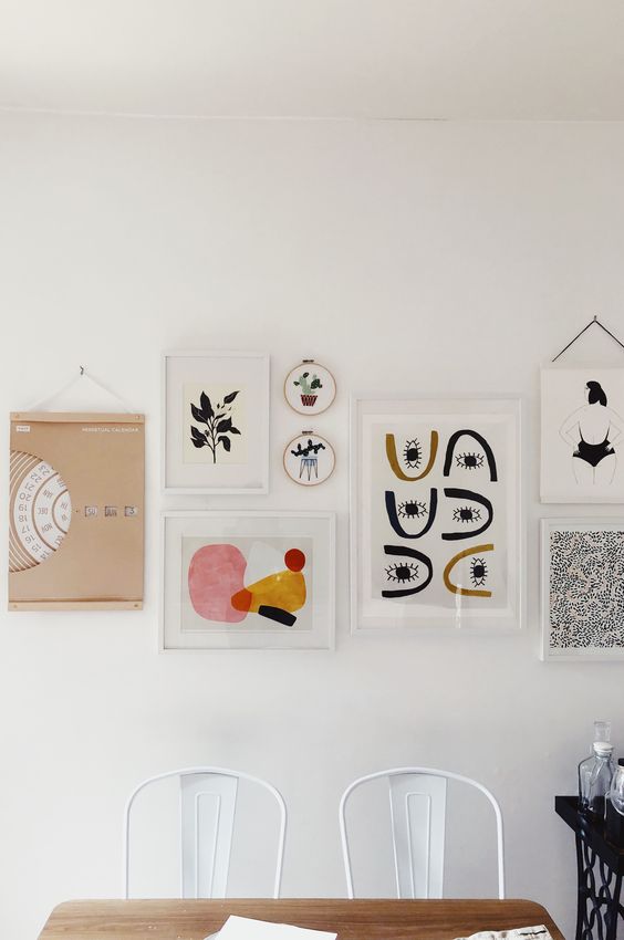An eye catchy gallery wall with white and blonde wood frames, with bold graphic artworks is chic and cool