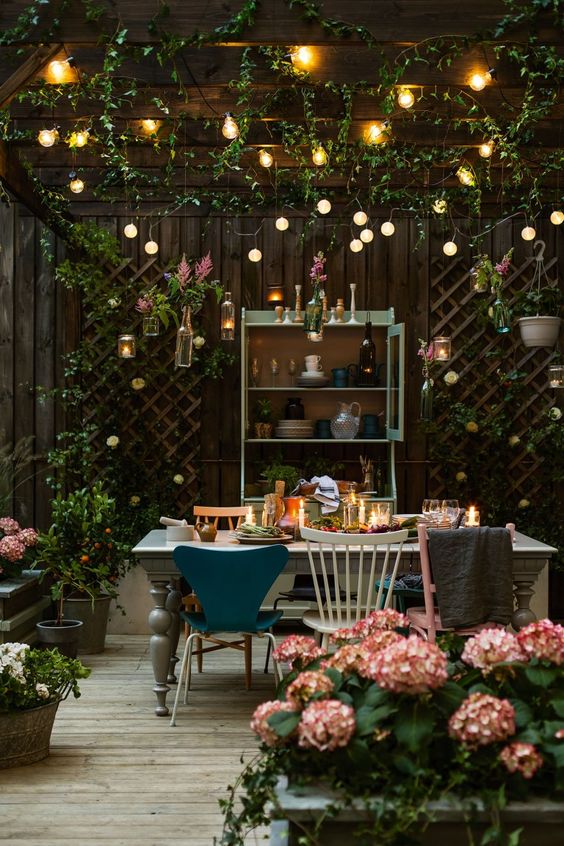 04 a backyard dining space with string lights over the space and candle lanterns on the table plus florals around