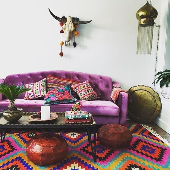 04 a colorful boho living room with a purple sofa, a colorful rug, bown poufs, a low table, a skull and a pendant lamp