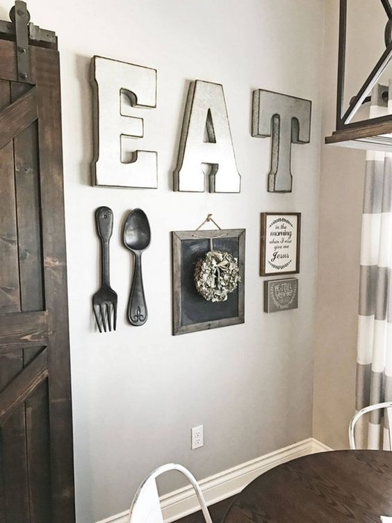 a pretty farmhouse kitchen gallery wall with large letters, metal cutlery, a couple of signs and a wreath on a chalkboard piece