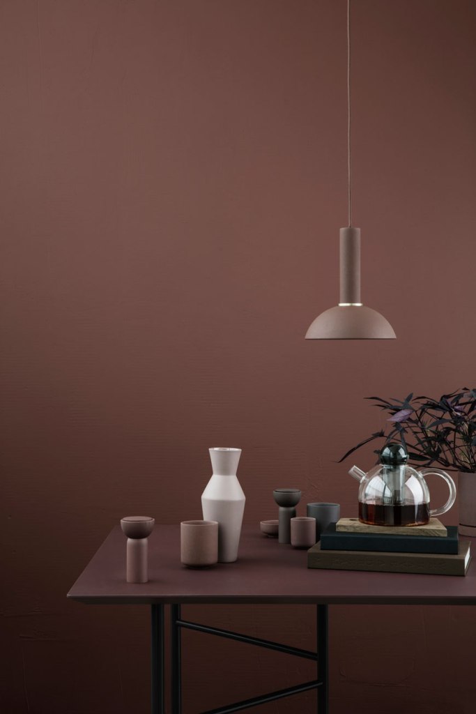 a stylish minimal space with a mauve wall and a matching mauve table, a taupe pendant lamp and porcelain