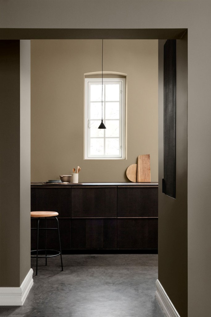 a minimalist kitchen done with olive green walls, sleek dark cabinetry, a black pendant lamp and light stained wood