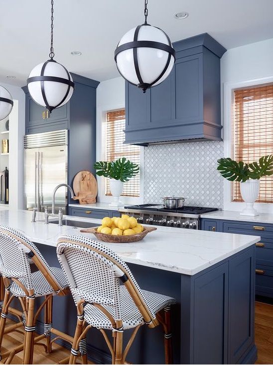 a cool tropical kitchen with blue cabinets and a matching hod, a tile backsplash, white stone countertops and catchy stools