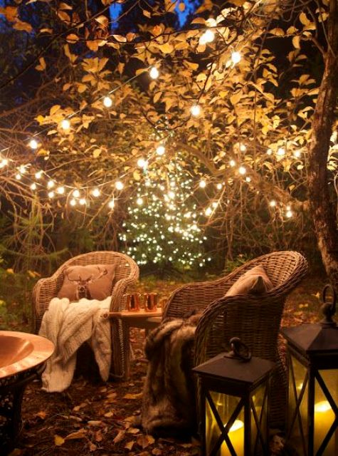 08 a cozy backyard with rattan chairs, lots of lights on the trees and candle lanterns and a fire pit is very inviting