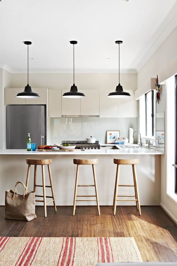a lovely ivory kitchen wiht sleek cabinets, white stone countertops and an integrated hood plus black pendant lamps