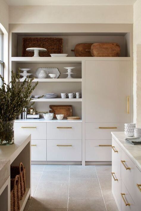 a lovely neutral kitchen with cool cabinets, gold handles, stone countertops and closed and opened storage units
