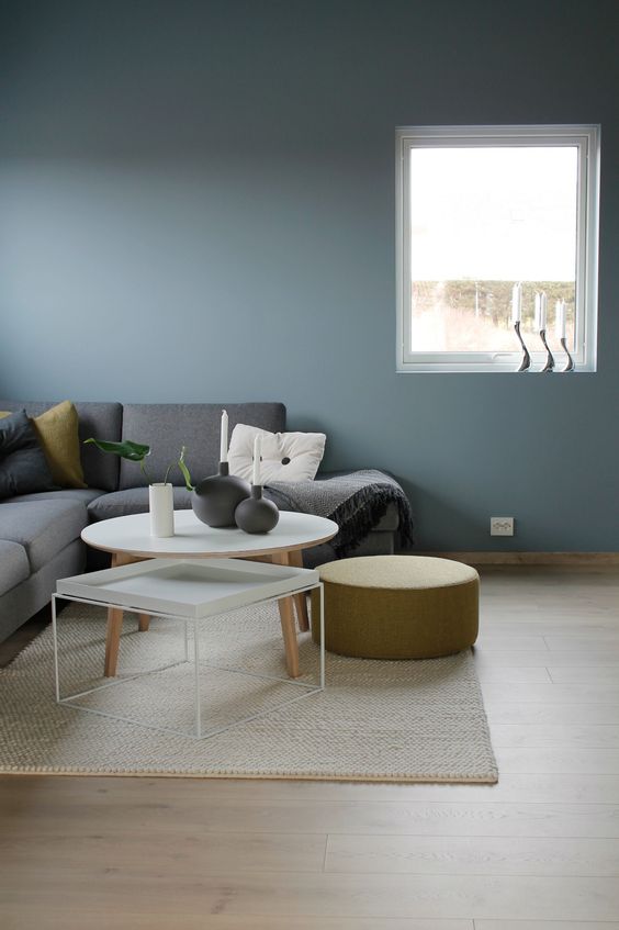 10 a minimalist Scandinavian space with blue walls, a grey sectional, mismatching tables and a round mustard ottoman