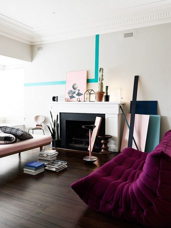 A contemporary living room with a non working fireplace, a blush couch and a deep purple sofa, color blocking and books