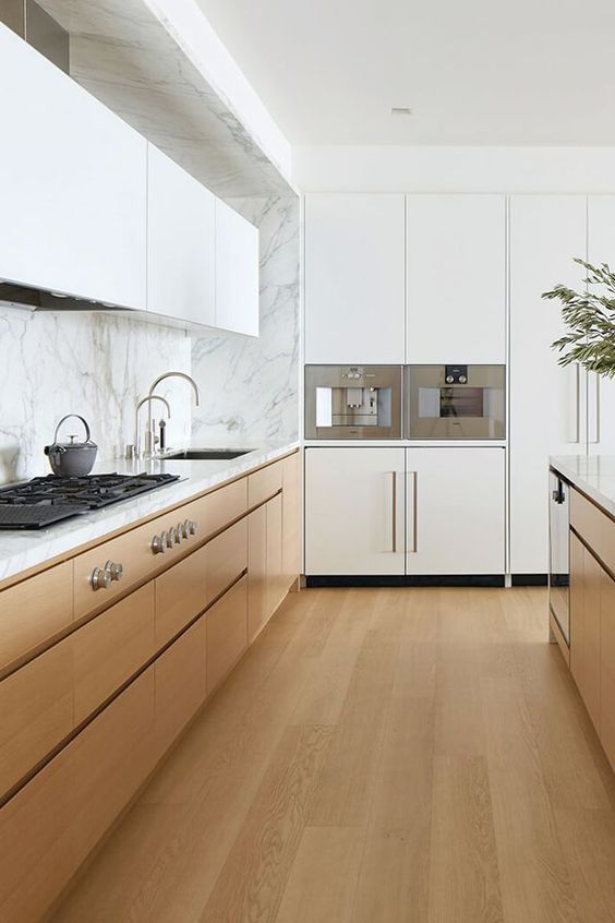 a minimalist two-tone kitchen with an incorporated hood and white marble countertops and a backsplash is welcoming