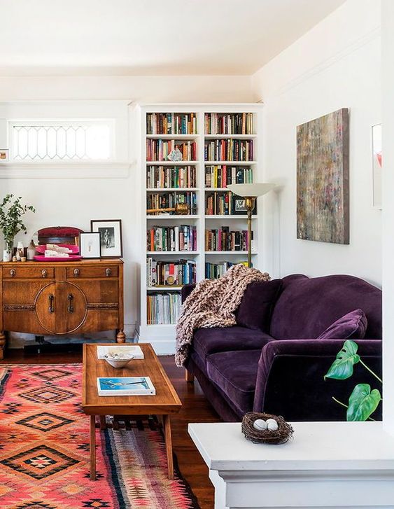 A mid century modern living room done in neutrals and filled with color   a printed rug, a deep purple sofa, stained furniture and a built in bookcase