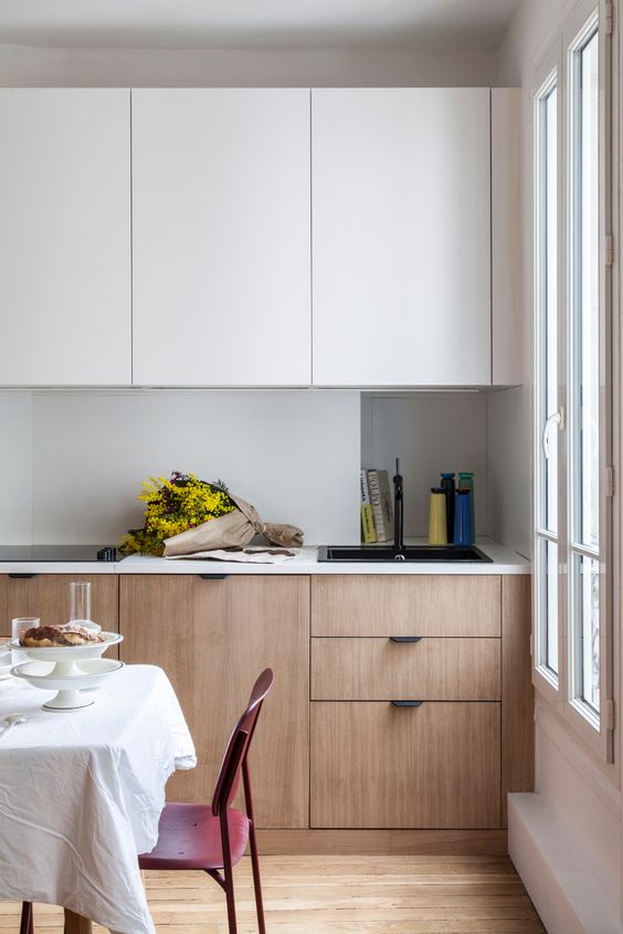a minimalist two-tone kitchen with sleek cabinets, an incorporated hood and white countertops and a backsplash is chic