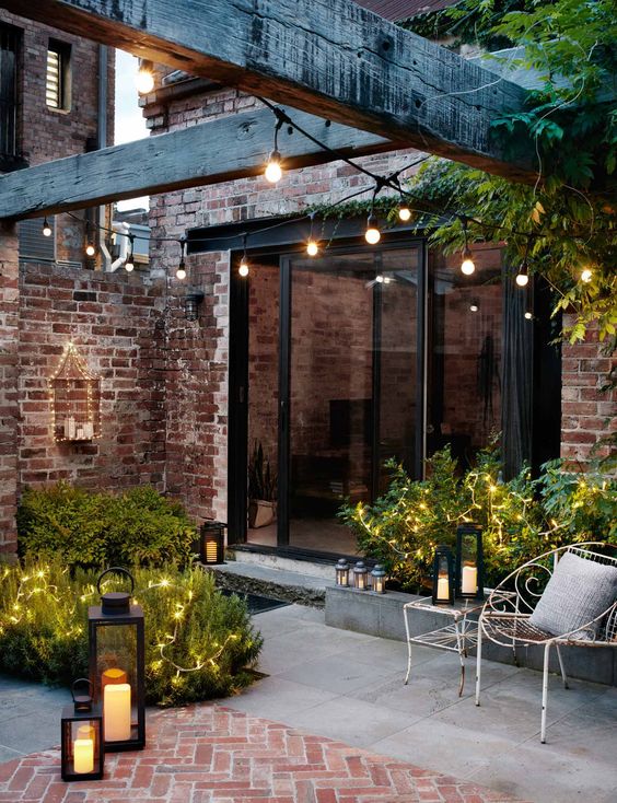 13 a refined backyard with fairy lights on plants, string lights over the space and candle lanterns all around