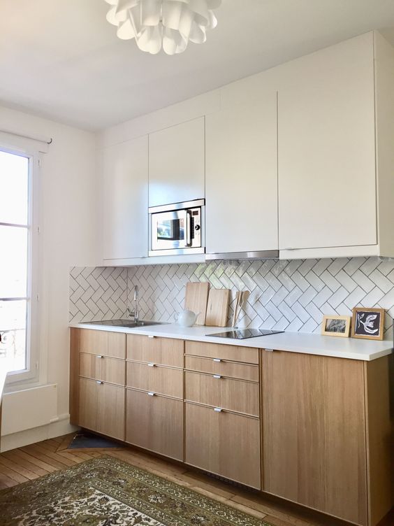 a modern kitchen with sleek white cabinetry and light stained lower ones plus a herringbone backsplash is lovely