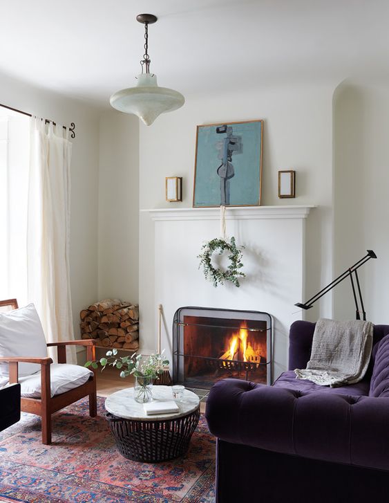 a beautiful neutral living room with a fireplace, a mantel with decor, a white chair and a gorgeous deep purple sofa and a round table