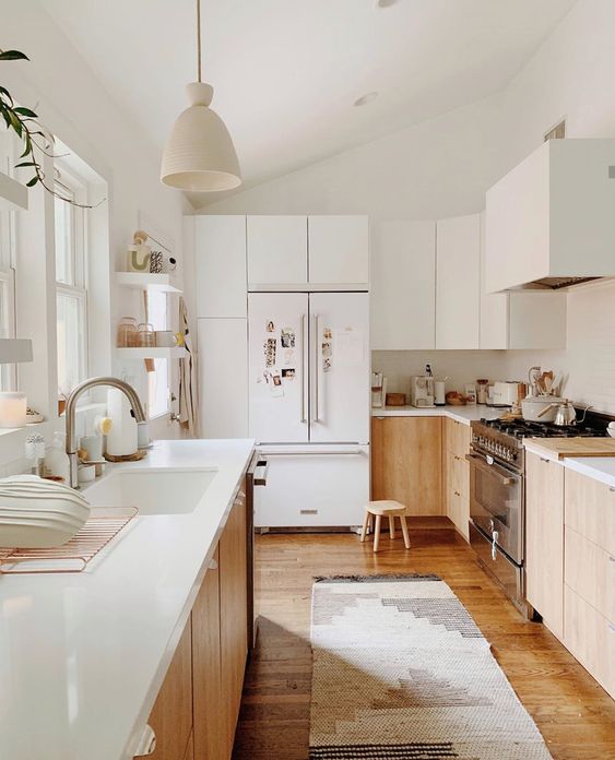 a neutral modern kitchen with light stained cabinets, white countertops and white upper cabinets plus a white hood that loosk seamless here