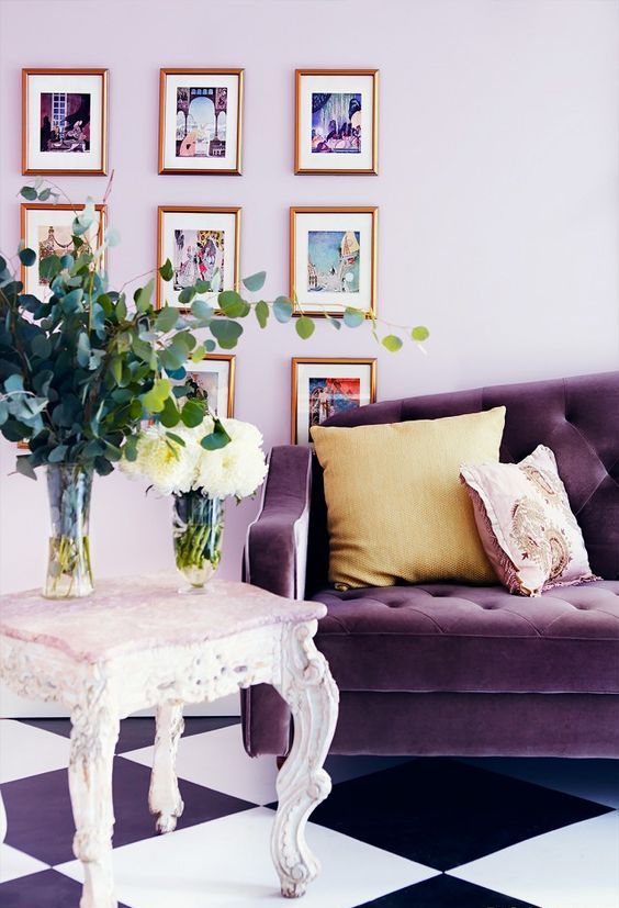 a chic living room with lilac walls, a purple sofa, a refined carved stool and a lovely gallery wall is wow