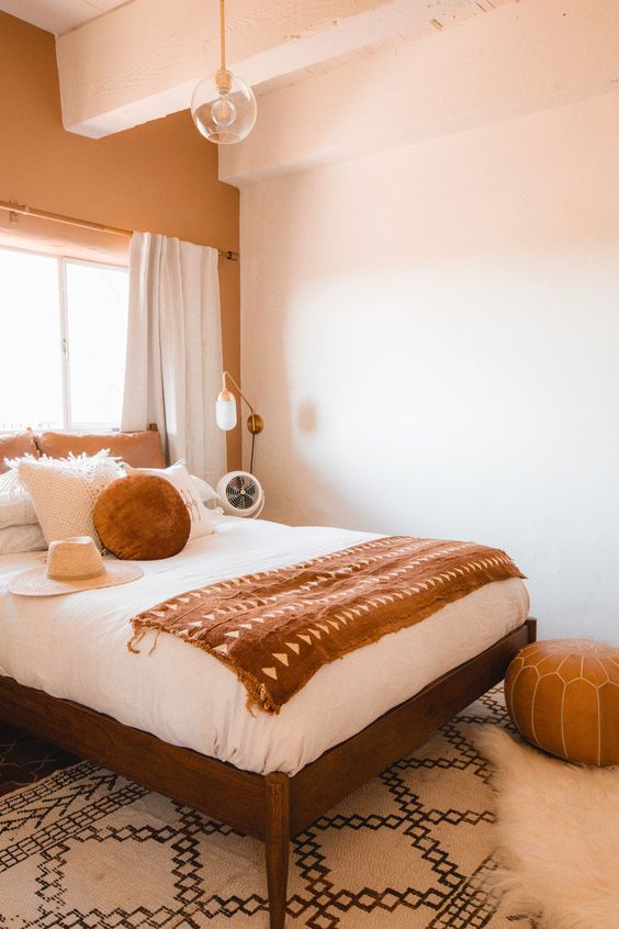 a small and cozy bedroom done in earthy tones, with rust and brown shades, a comfy bed, a leather pouf and cool bulbs