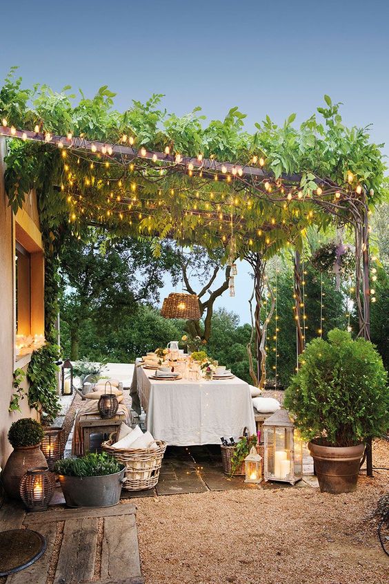 19 an outdoor dining zone with wooden furniture, baskets, potted greenery, candle lanterns and lights creatign a canopy over the space