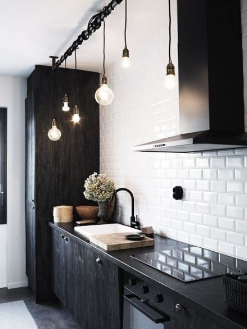 a modern Scandinavian black and white kitchen with a white subway tile backsplash and black cabinetry and cool bulbs