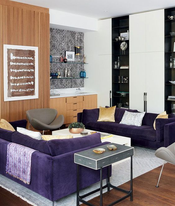 a contemporary living room with two purple sofas, grey chairs, light stained and black and white storage furniture