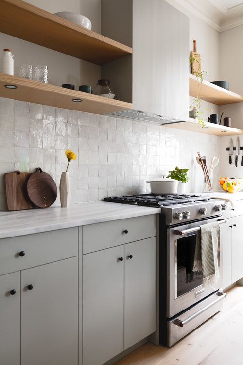 a stylish contemporary kitchen with grey cabinets and a matching hood and built-in shelves plus a white tile backsplash