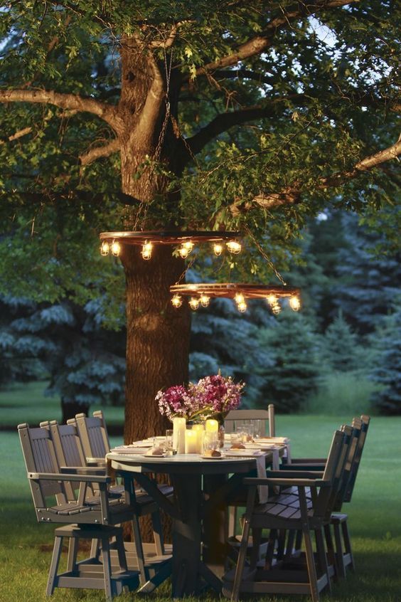an outdoor dining area with rustic wooden furniture, candles on the table and rustic bulb chandeliers is amazing
