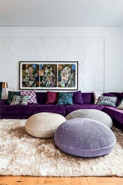 22 a cool living room done in neutrals, with a large purple sectional, a bold artwork, colorful pillows and a trio of poufs