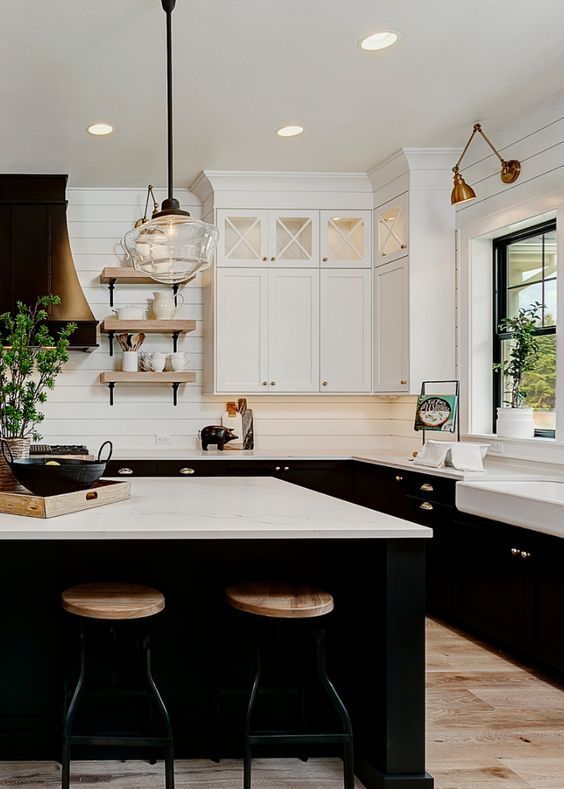a stylish black and white farmhouse kitchen withwhite beadboard walls, black cabinetry, a metal hood and touches of blonde wood