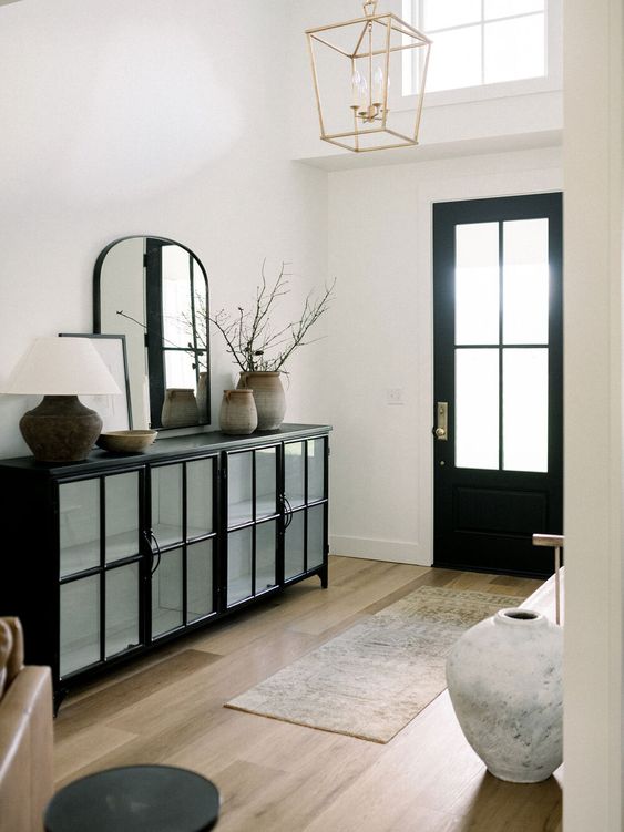a refined entryway in black and white, with a black storage unit, a curved mirror, a rug, a bench, a black door and a pendant lamp