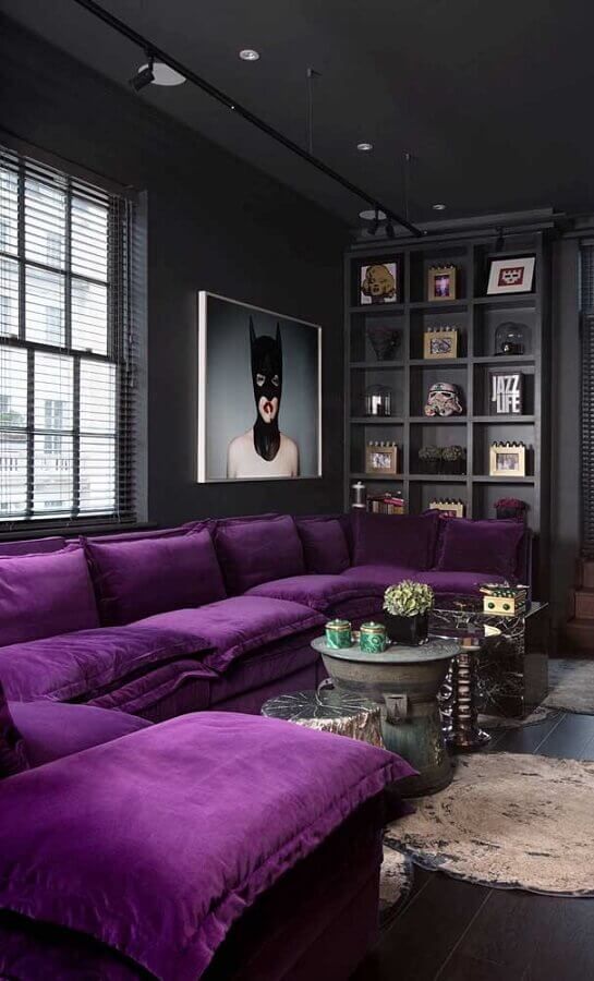 A moody contemporary living room done in black and graphite grey, a built in shelf for displaying, a purple sectional and a statement artwork