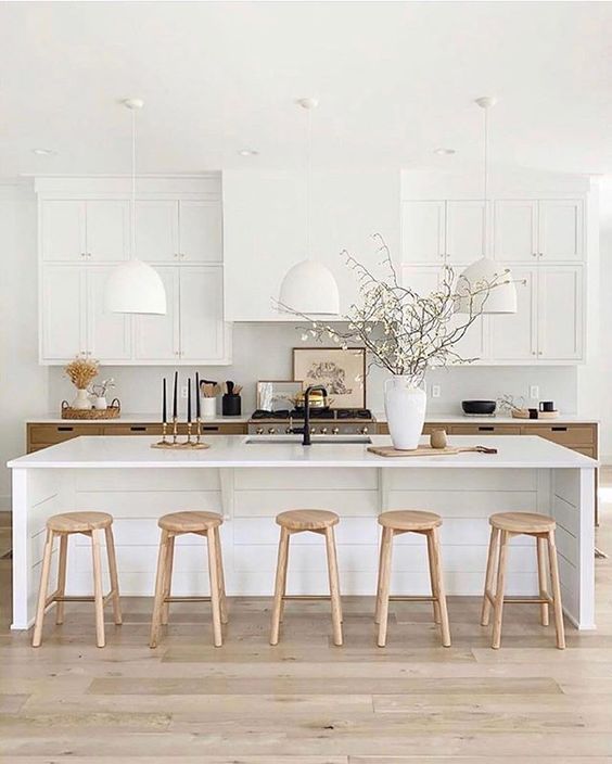 an elegant white farmhouse kitchen with a hood that matches the upper cabinets, white stone countertops and pendant lamps