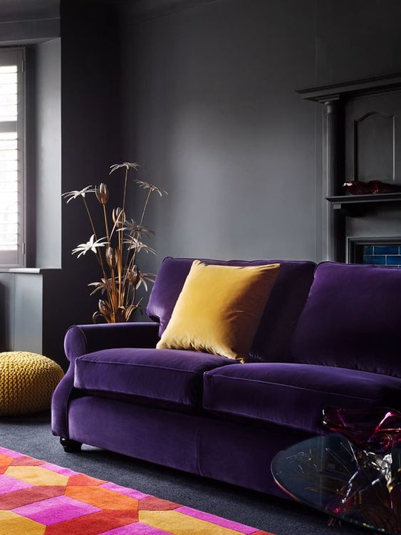 25 a moody living room in dark greys spruced up with a deep purple sofa, yellow pillows and a colorful geometric rug