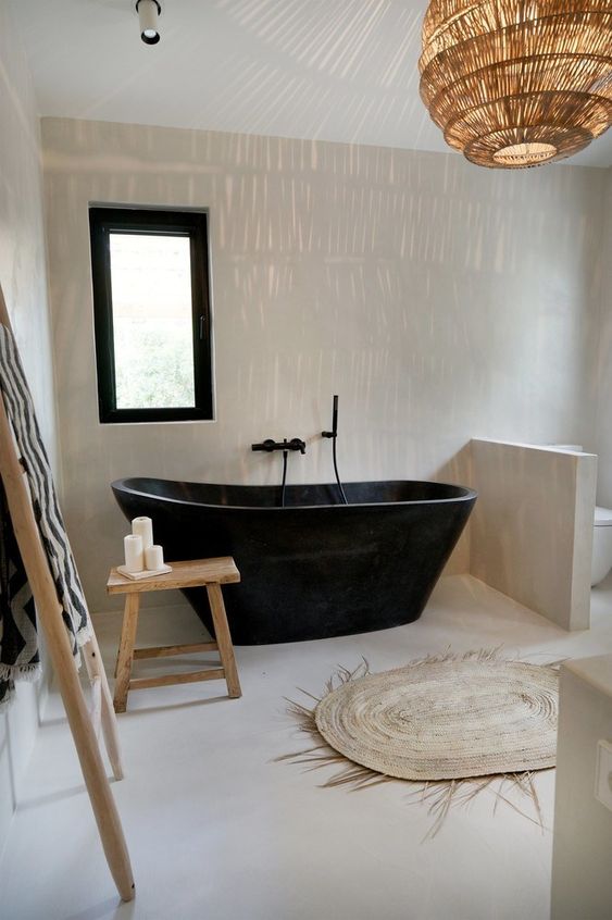 a beautiful natural bathroom in neutrals, with a black bathtub and a black framed window, a rattan lamp and a jute rug