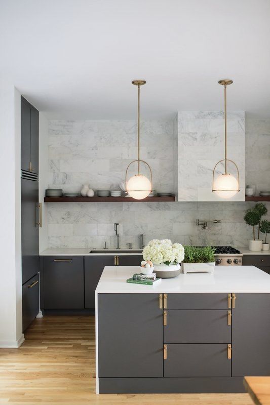 a chic modern kitchen with grey cabinetry, gold touches, white countertops, white marble tiles on the backsplash and a hood plus pendant lamps