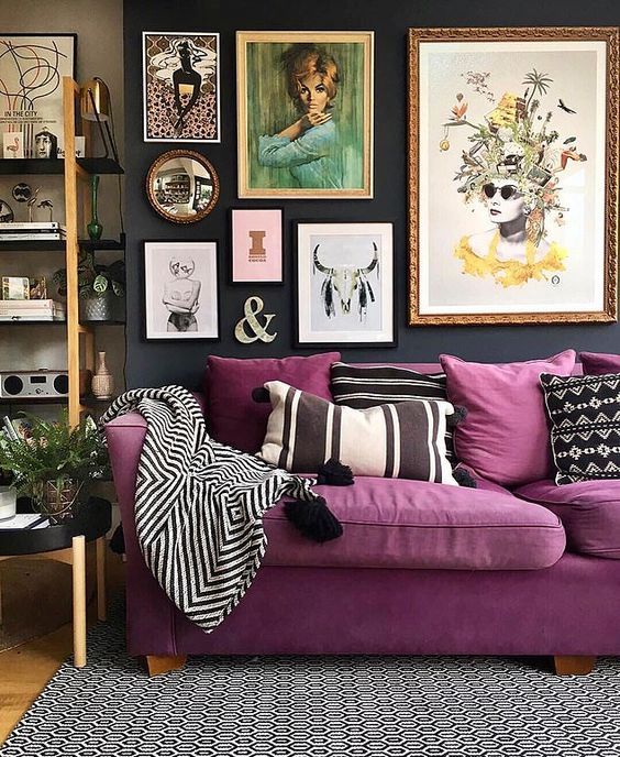 a moody living room with a purple sofa, an open shelving unit and a bright gallery wall plus printed pillows is cool