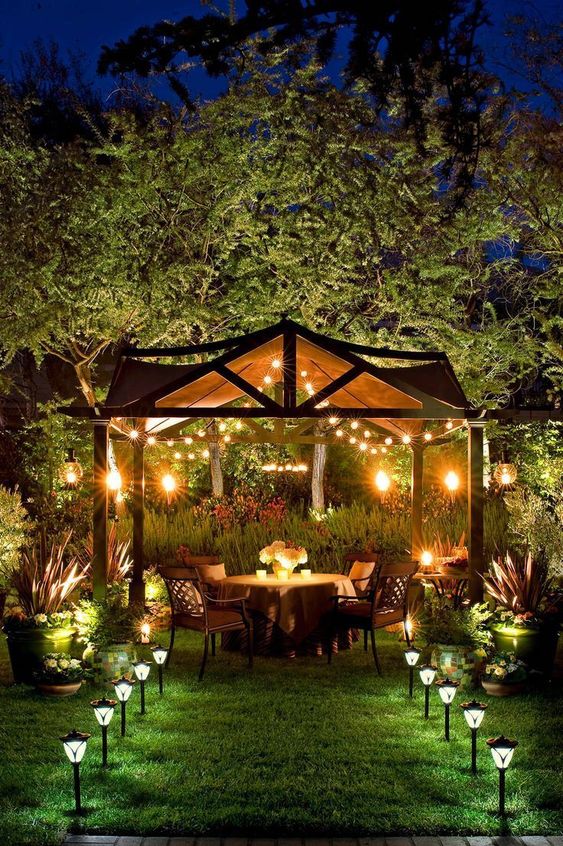 27 a backyard dining zone with lights over the space and outdoor lamp lining up the path looks very welcoming