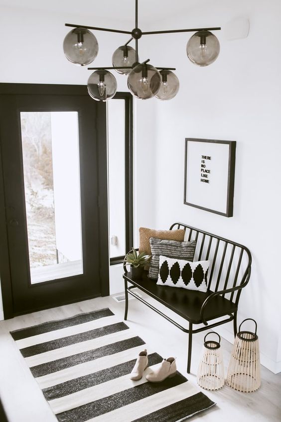 a chic Scandinavian entryway with a black bench, a striped rug, candle lanterns, printed rugs and a catchy chandelier
