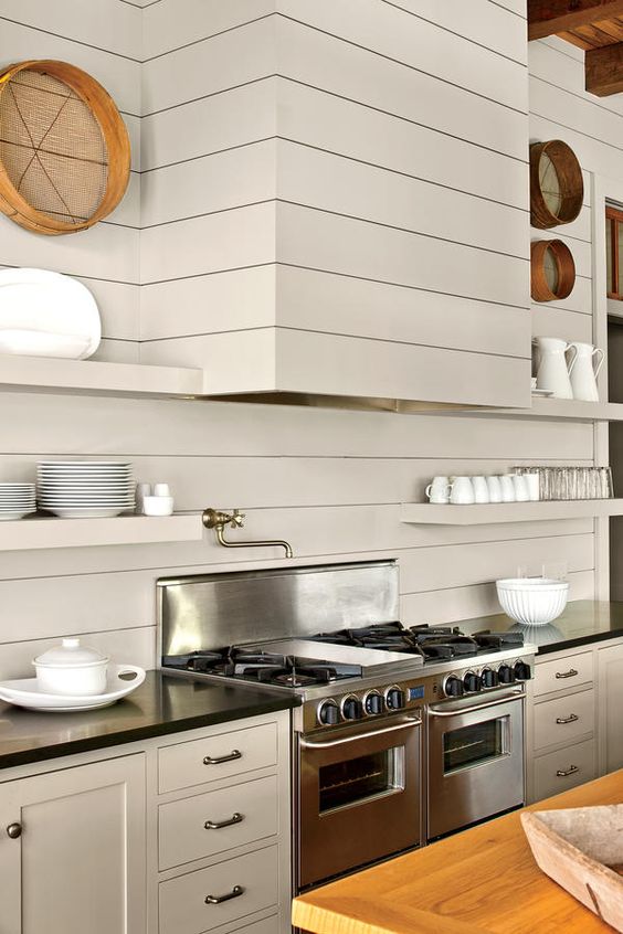 a creative modern kitchen done with ivory beadboards, black countertops, metal appliances and a seamless hood and shelves
