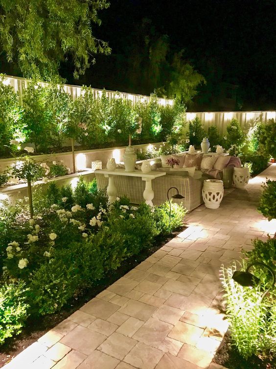 a lit up backyard with outdoor garden lamps all around, hidden and not, is a very welcoming garden space